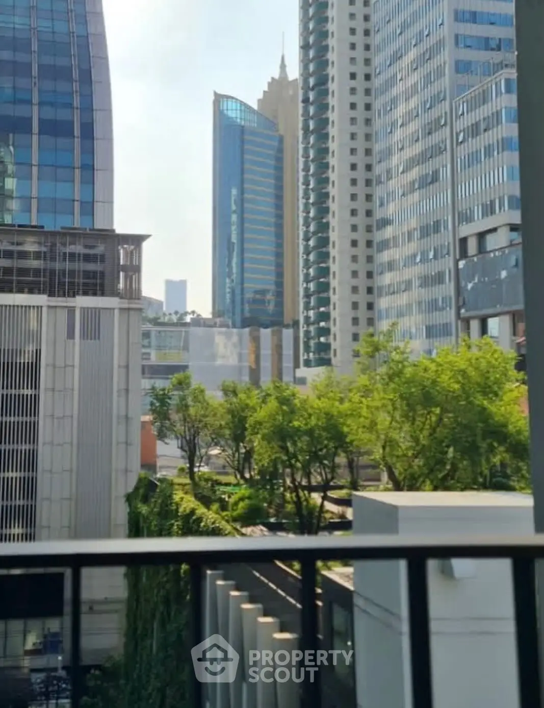 Stunning urban view from a balcony overlooking modern skyscrapers and lush greenery.