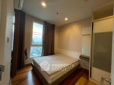 Cozy bedroom with city view, featuring a large window and wooden flooring, perfect for urban living.