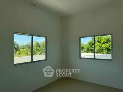 Bright room with two windows offering lush green views, perfect for a serene living space.