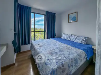 Cozy bedroom with large window and blue floral bedding, offering a serene view.