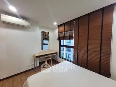 Modern bedroom with large window and wooden blinds, featuring a minimalist desk and air conditioning.