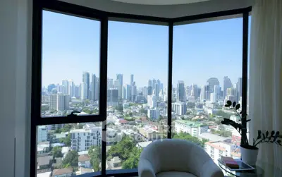 Stunning cityscape view from a modern high-rise apartment with large windows and cozy seating area.