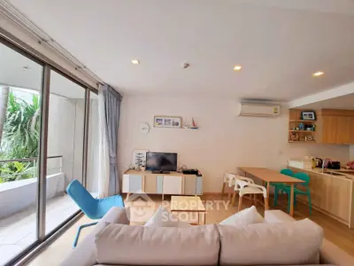 Modern living room with open kitchen and balcony view, featuring stylish furniture and natural light.