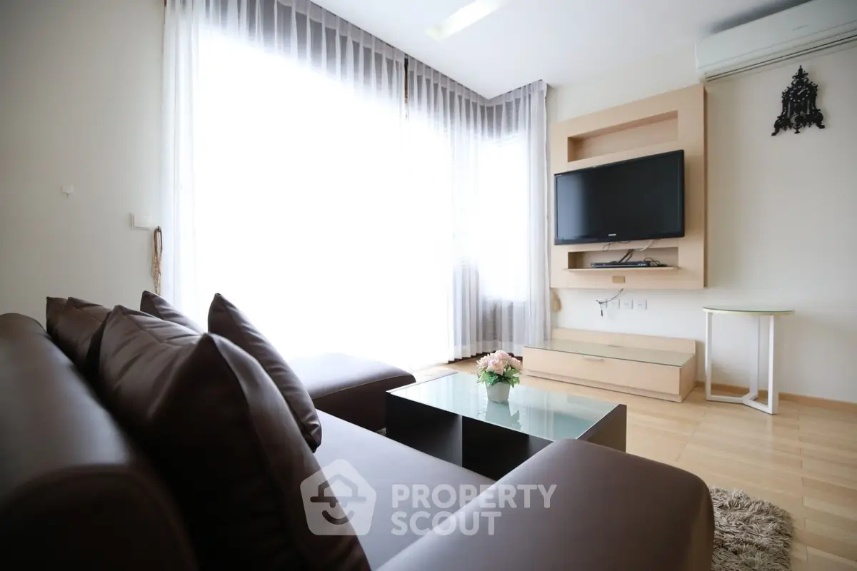Modern living room with sleek furniture and natural light, featuring a wall-mounted TV and stylish decor.
