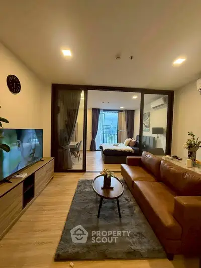 Modern living room with leather sofa and TV, open layout to dining area with city view.