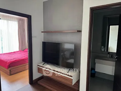 Modern apartment interior with bedroom and TV area, featuring sleek wooden furniture and natural light.