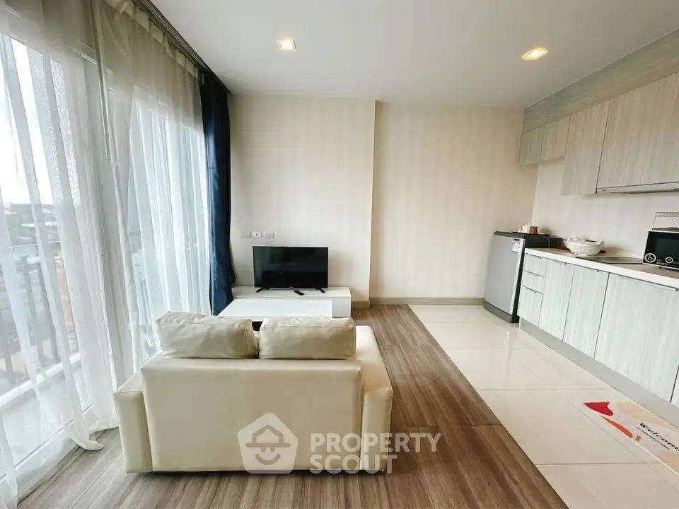 Modern living room with open kitchen, featuring sleek cabinetry and cozy seating area.