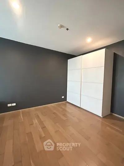 Spacious bedroom with sleek wooden flooring and modern wardrobe in a contemporary apartment.