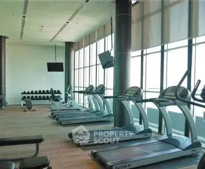 Modern gym with treadmills and weights in a high-rise building, offering a bright and spacious workout area.