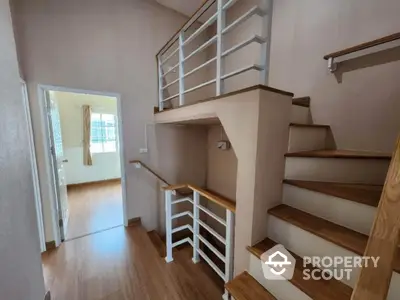 Modern staircase with wooden steps and white railings leading to a bright room with wooden flooring.