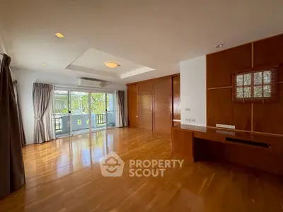 Spacious living room with wooden flooring and large windows offering natural light and garden view.