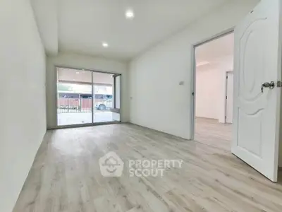 Spacious empty room with wooden flooring and sliding glass doors leading to a patio.