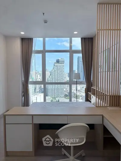 Modern bedroom with city view, featuring sleek desk and chair, large window, and stylish decor.