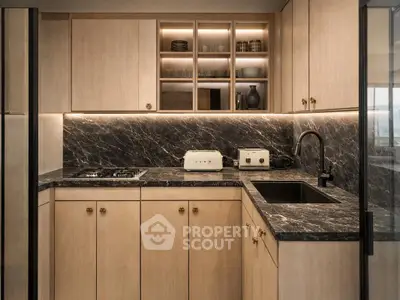 Modern kitchen with sleek black marble countertops and light wood cabinetry, featuring built-in gas stove and elegant lighting.