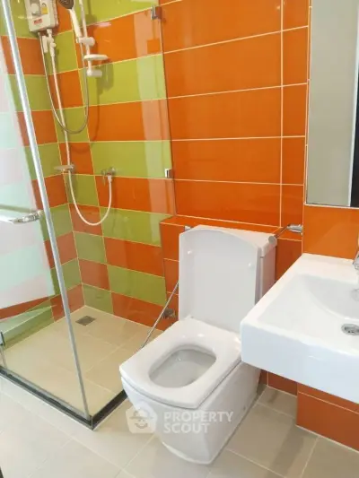 Modern bathroom with vibrant orange and green tiles, glass shower, and sleek fixtures.