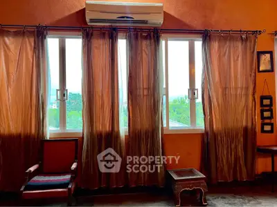 Cozy living room with large windows and elegant curtains, featuring a classic armchair and side table.