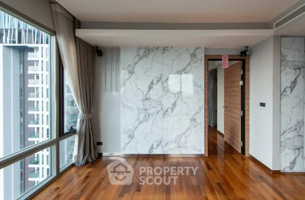 Spacious modern living room with marble accent wall and large windows offering city views.
