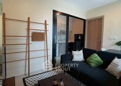 Modern living room with sleek black sofa and open kitchen layout in stylish apartment.