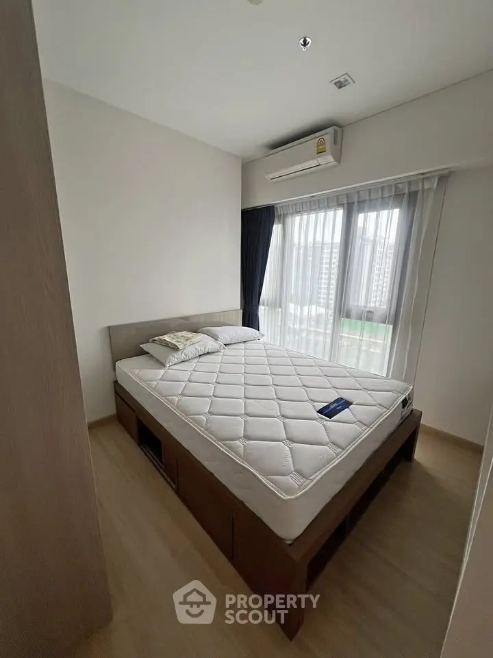 Cozy bedroom with large window and modern air conditioning unit, perfect for city living.