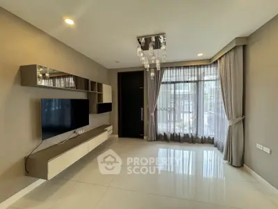 Modern living room with sleek TV setup and elegant chandelier lighting.