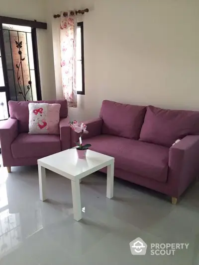 Cozy living room with plush mauve sofas and a sleek white coffee table, complemented by warm natural light and elegant curtains.