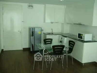 Modern kitchen with sleek white cabinets, compact dining area, and integrated appliances in a cozy apartment.