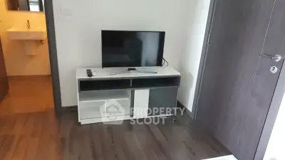 Modern living room with sleek TV stand and flat-screen TV, adjacent to a stylish bathroom entrance.