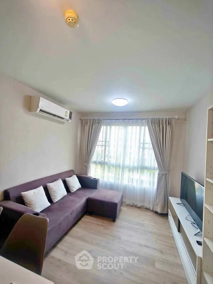 Cozy living room with modern sofa, air conditioning, and natural light from large window.