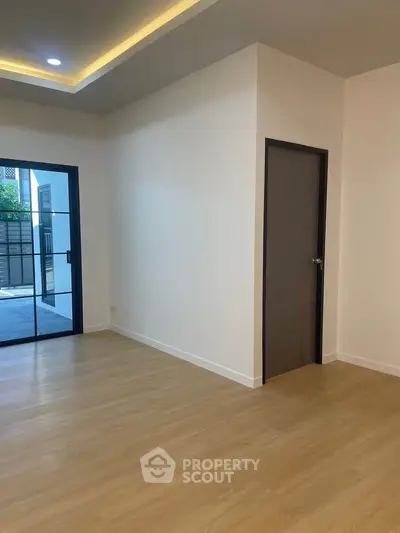Spacious modern room with wooden flooring and sliding glass doors leading to outdoor area.