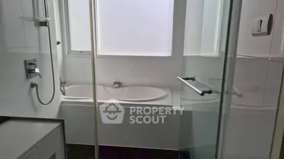 Modern bathroom with sleek glass shower and bathtub, featuring contemporary fixtures.