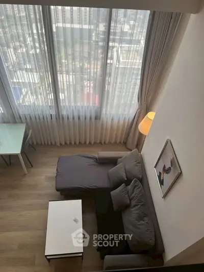 Modern living room with large windows offering stunning city views, featuring a cozy sofa and stylish decor.