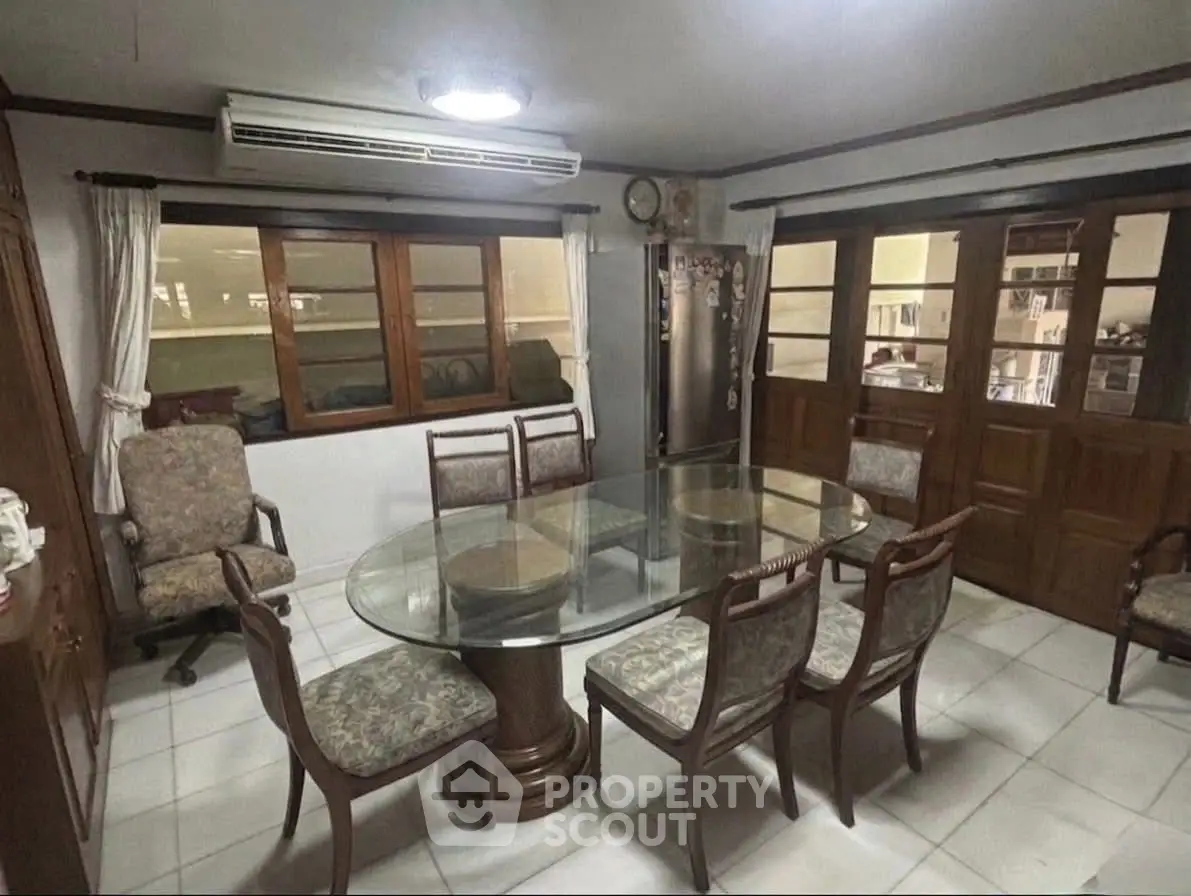 Spacious dining room with elegant glass table and wooden chairs, featuring large windows and air conditioning.