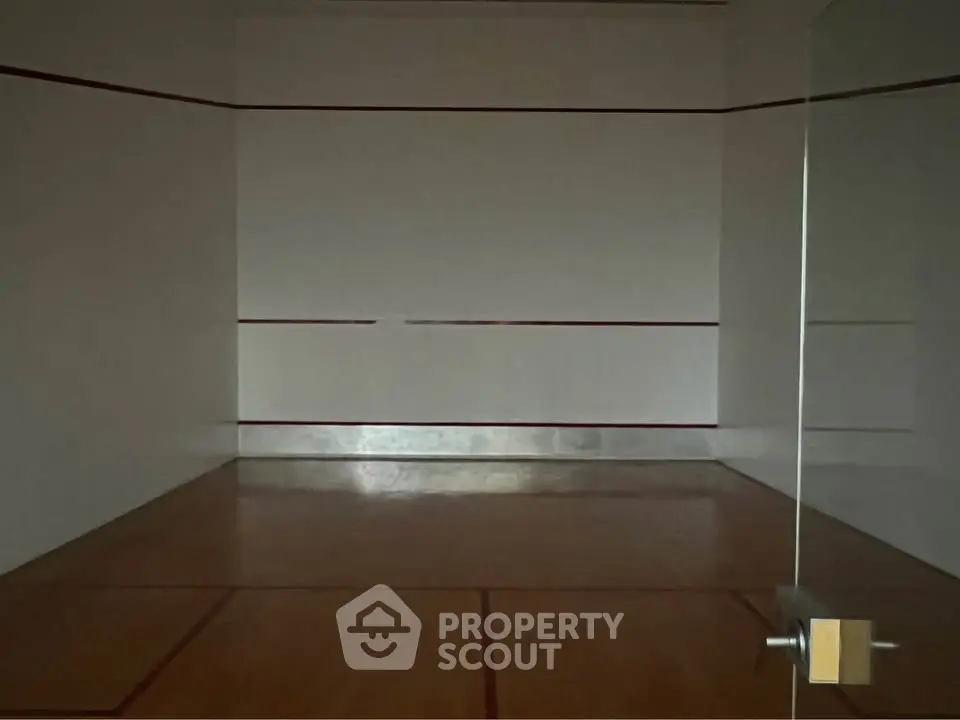 Spacious indoor squash court with wooden flooring and glass door, perfect for sports enthusiasts.