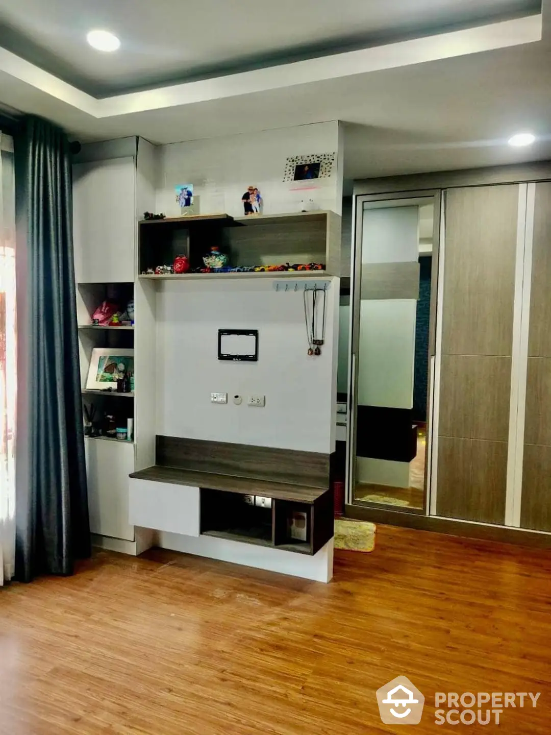 Cozy and inviting living space with custom shelving unit, warm wooden flooring, and modern lighting, perfect for comfortable urban living.