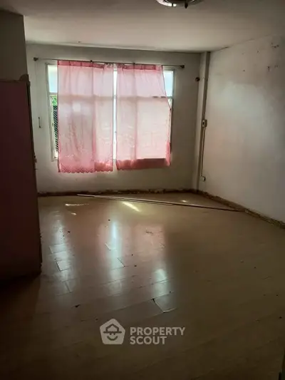 Spacious empty room with wooden flooring and large window, ideal for customization.