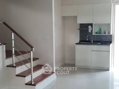 Modern minimalist kitchen with sleek cabinetry and staircase in a bright open space.