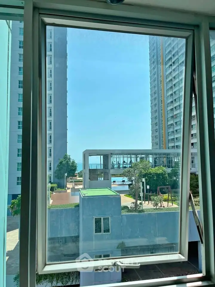 Stunning view from a high-rise apartment window overlooking modern urban landscape and pool area.