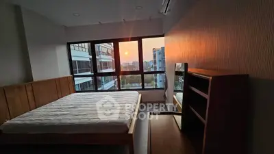 Spacious bedroom with large windows offering stunning sunset views in modern apartment.