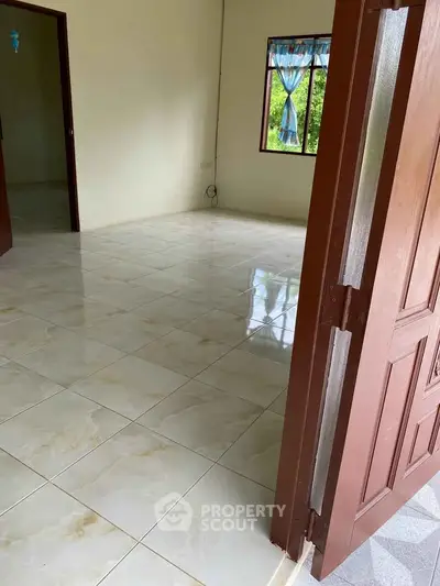 Spacious tiled room with open wooden door and natural light