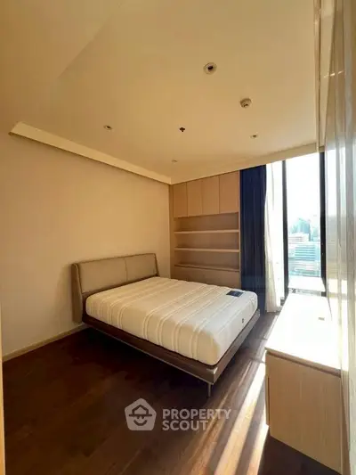 Modern bedroom with large window and built-in storage, featuring a minimalist design and natural light.
