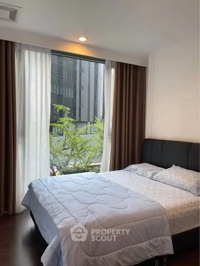 Modern bedroom with large window and city view, featuring cozy bedding and elegant curtains.