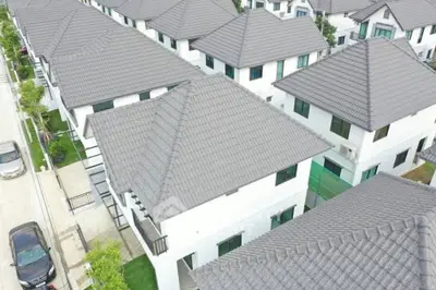 Aerial view of a modern residential housing complex with uniform white houses and grey tiled roofs, showcasing the neat arrangement and suburban appeal.