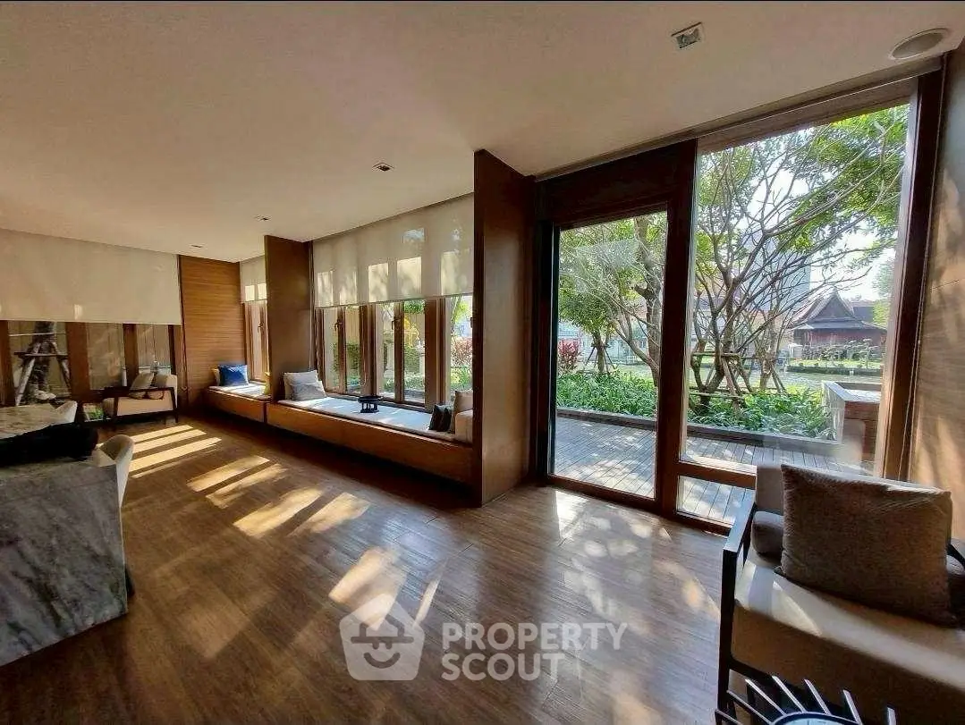 Spacious living room with large windows and garden view, featuring elegant wooden flooring and modern decor.