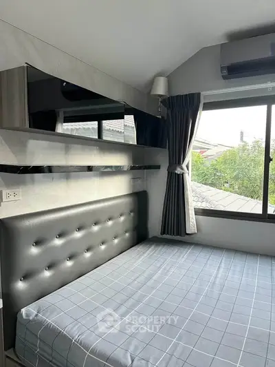 Modern bedroom with stylish decor and large window offering natural light and outdoor view.