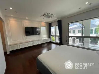 Spacious bedroom with polished hardwood floors, large windows offering ample natural light, and built-in white cabinetry surrounding a modern entertainment unit.