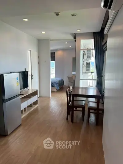 Modern apartment interior with open layout, featuring dining area and view into bedroom.