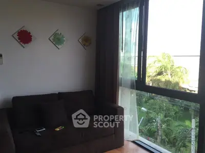 Cozy living room with large window and garden view, featuring a comfortable sofa and floral wall art.