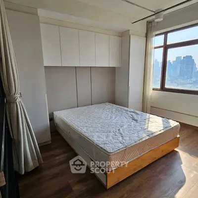 Bright bedroom with city view and built-in storage, featuring a comfortable bed and large window.