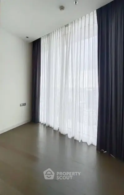 Spacious empty room with floor-to-ceiling windows and elegant curtains