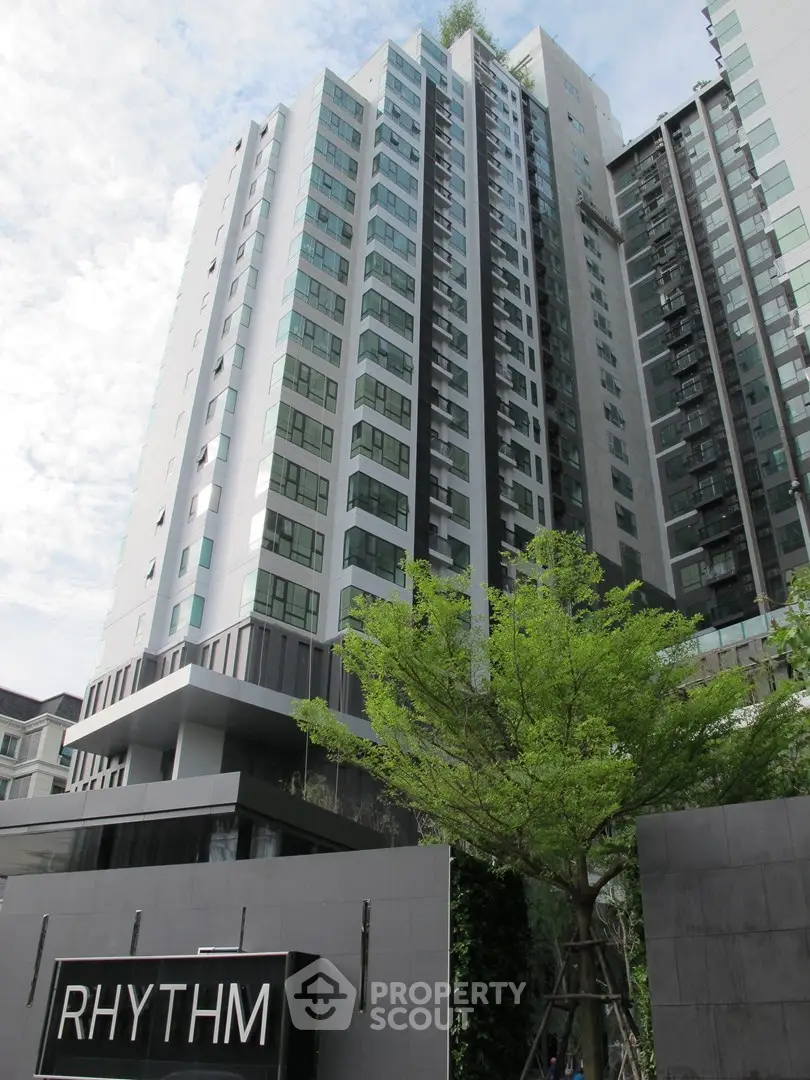 Modern high-rise condominium building with sleek design and lush greenery in urban setting.